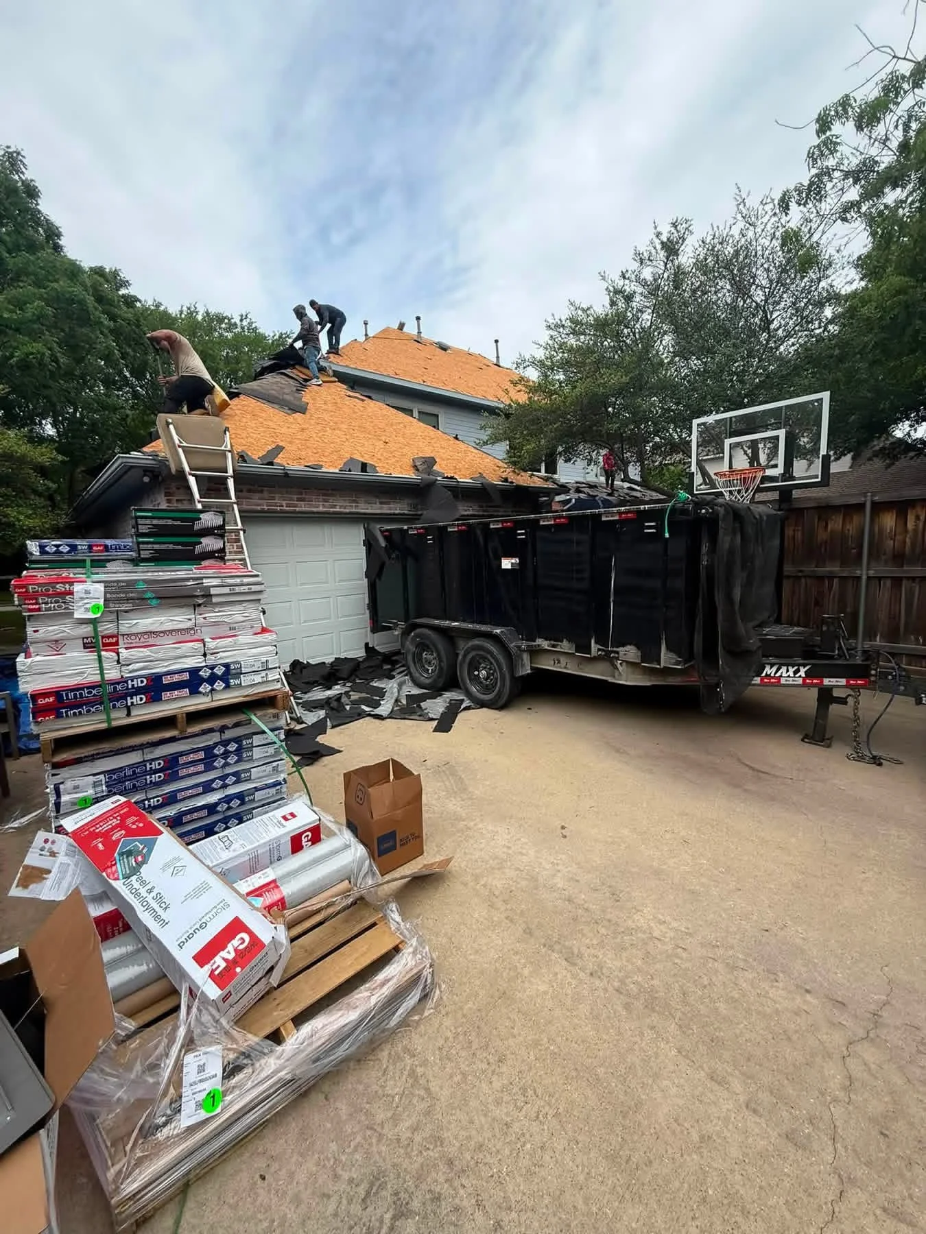 Residential roof replacement with new orange architectural shingles, crew installing materials on multi-plane roof