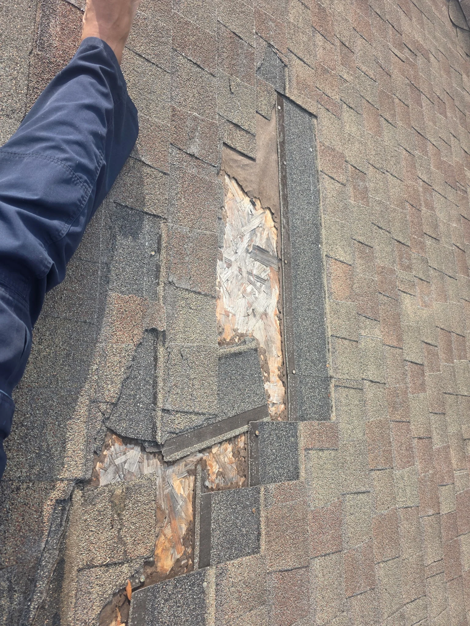 Damaged asphalt shingles with exposed wood and deteriorated flashing on roof edge
