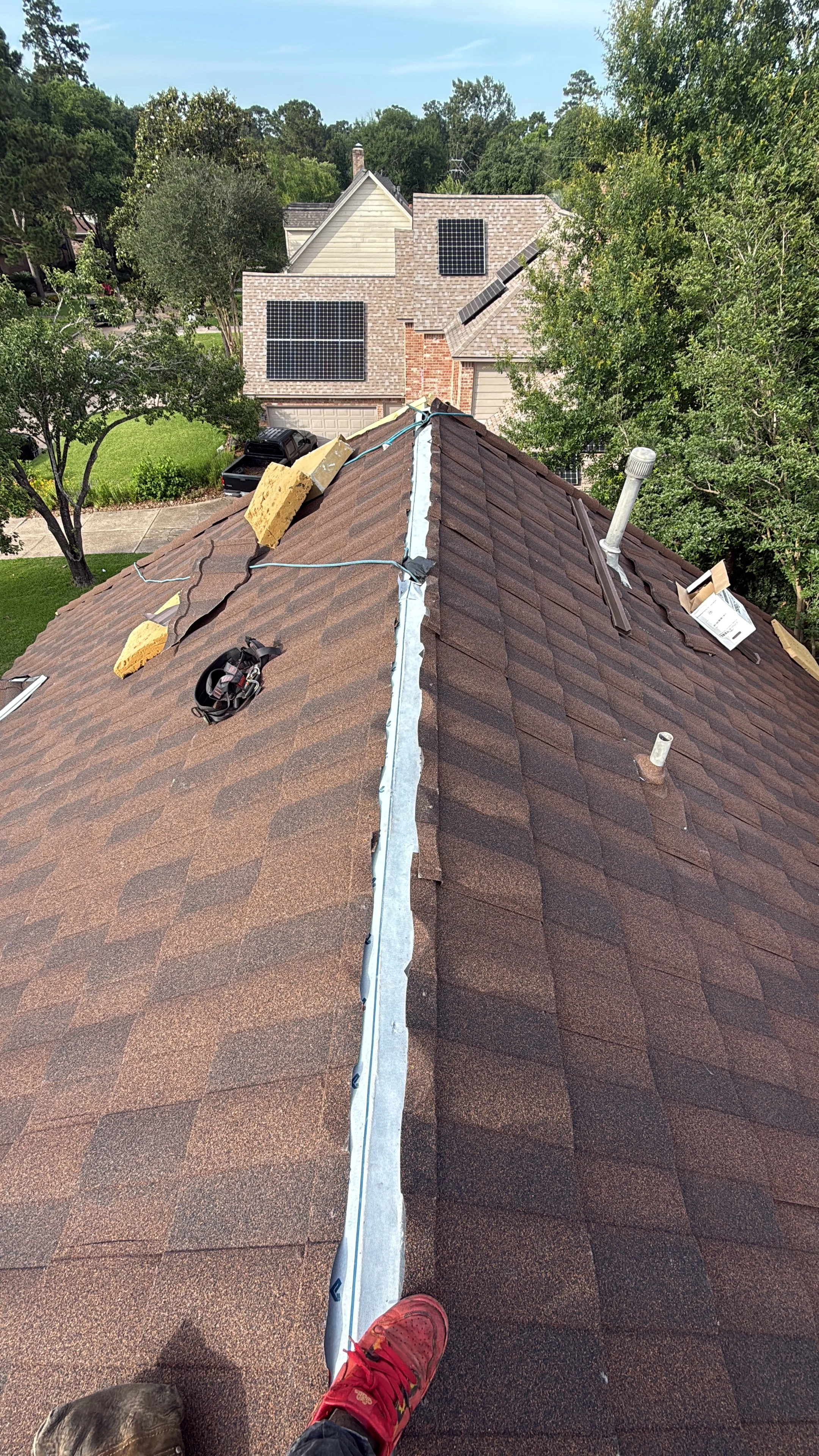 Roofer installing dark brown architectural shingles with metal ridge flashing on residential roof