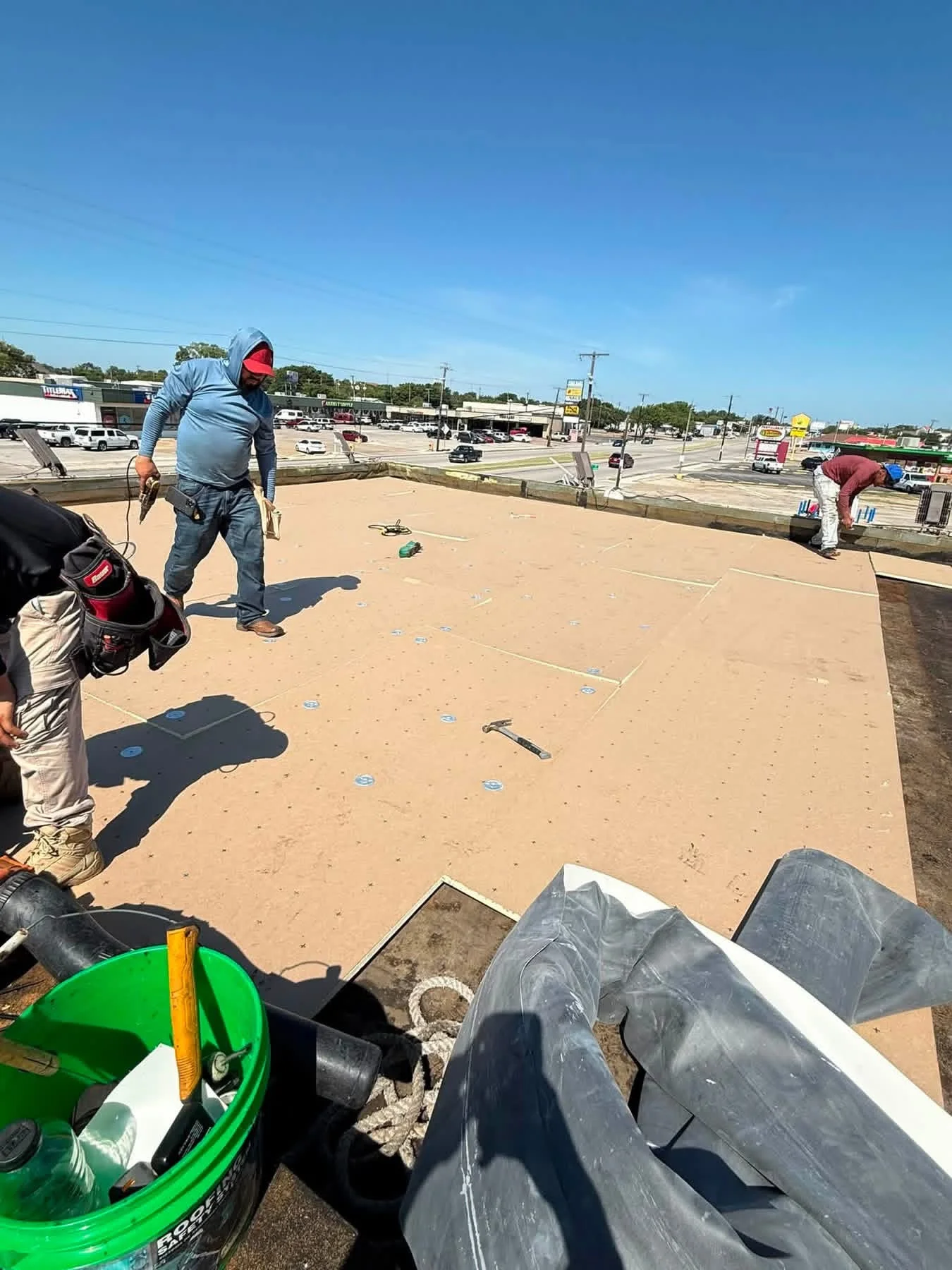 Workers installing tan flat roof membrane with fasteners on large commercial building