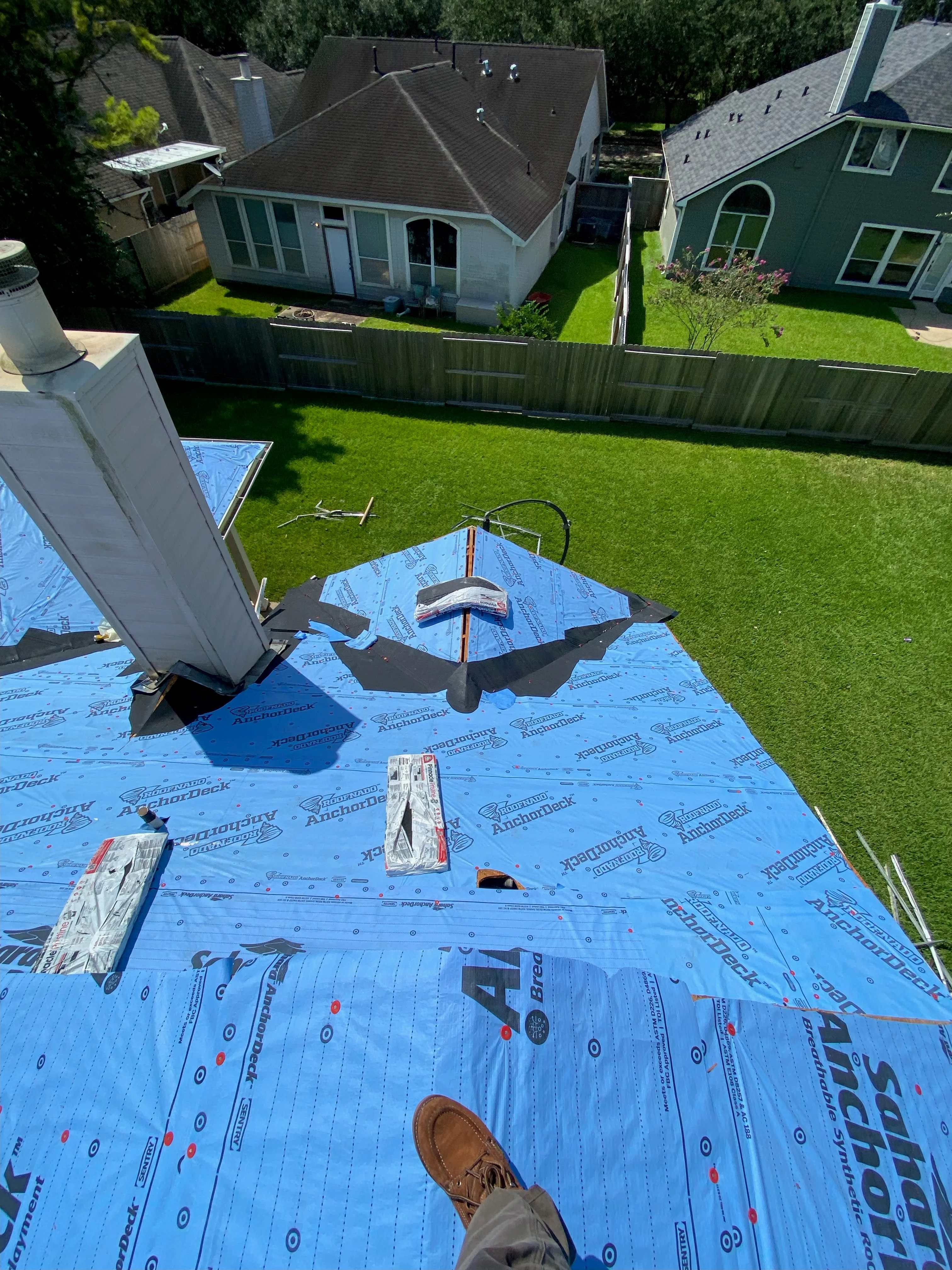 Roof replacement in progress with blue underlayment and asphalt shingles on residential home