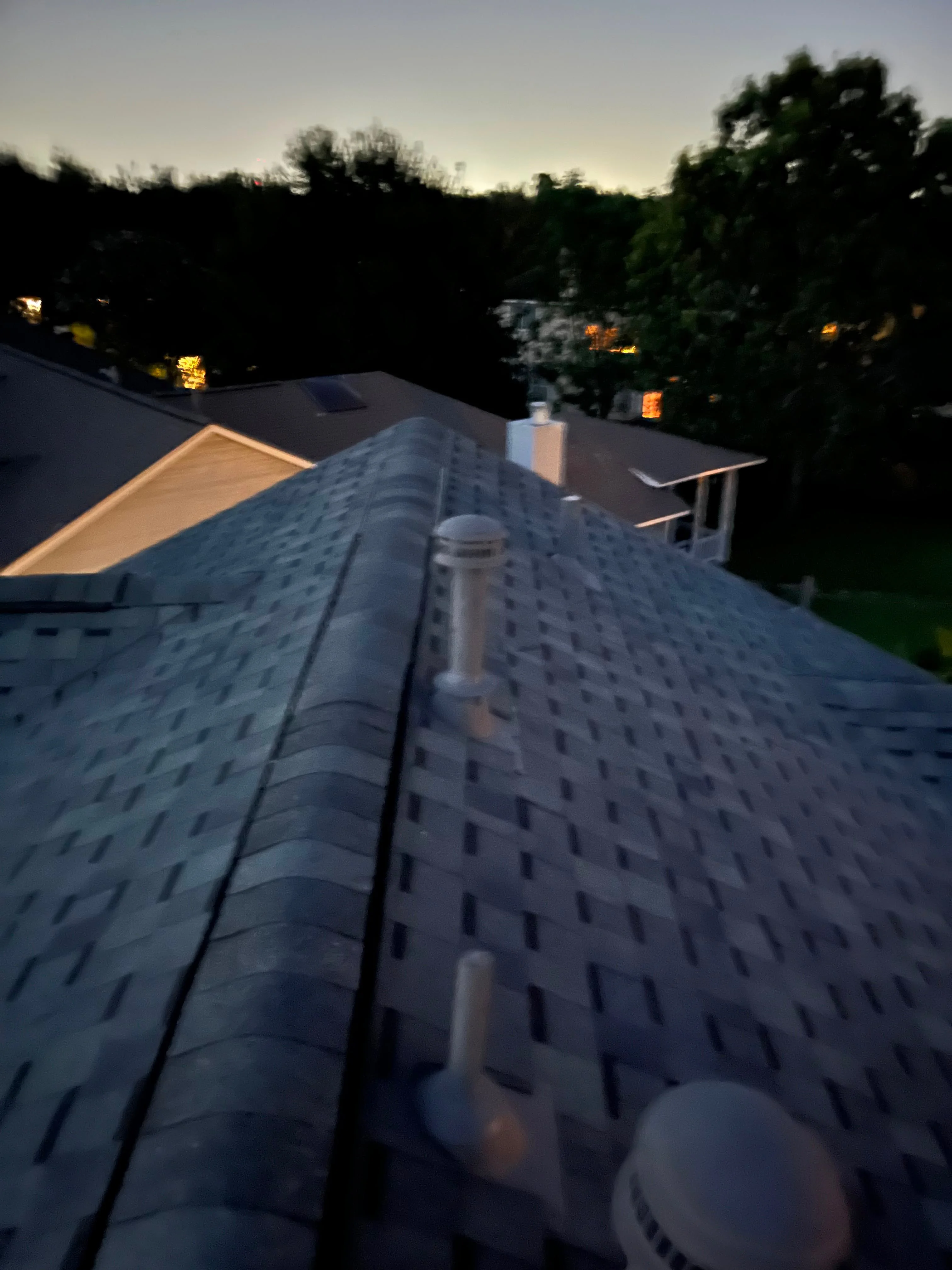 Newly installed architectural shingles with chimney flashing and ridge vent on residential roof