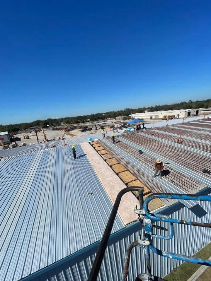 Corrugated metal roof installation on commercial building with multiple sections and workers
