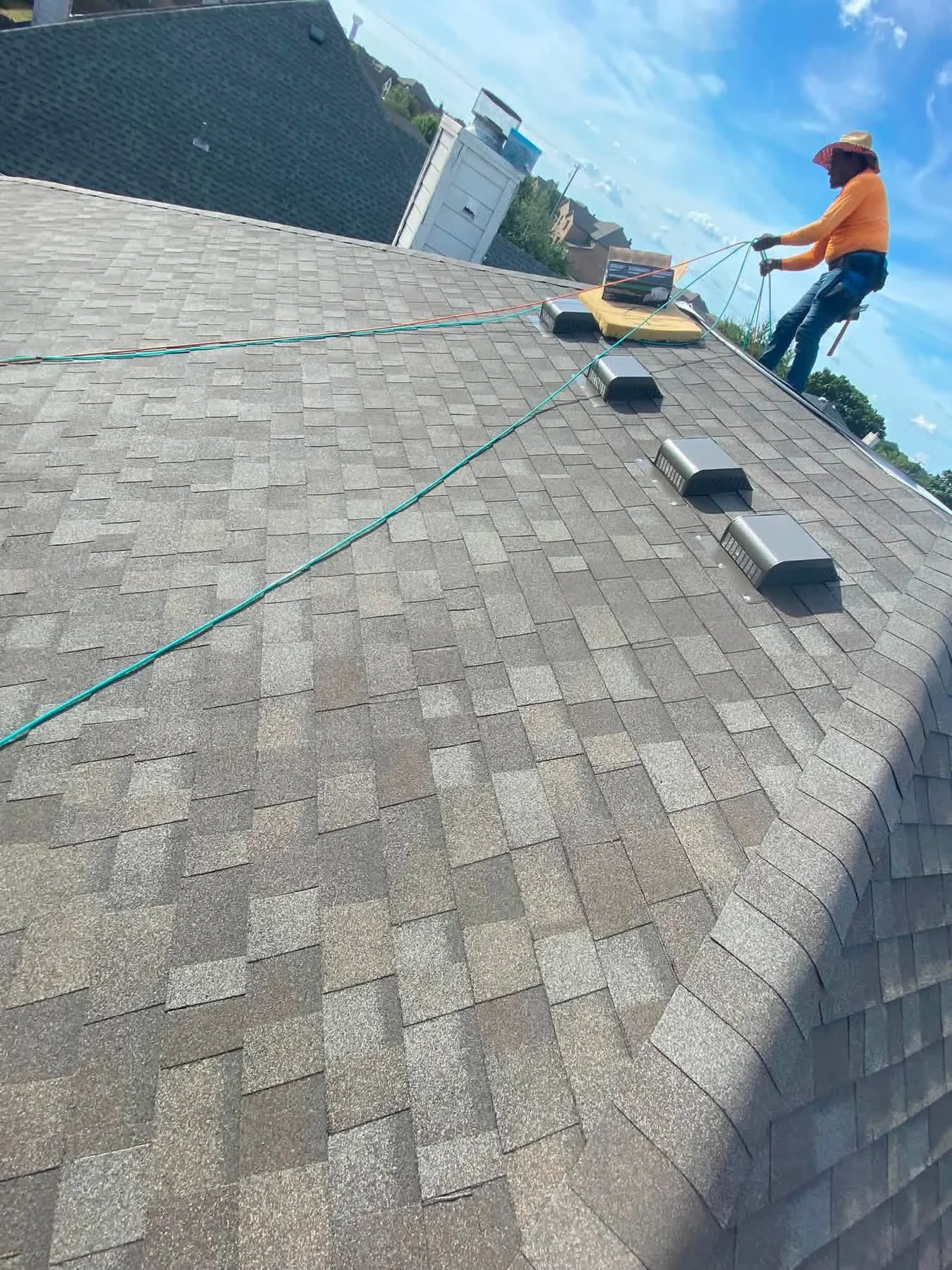Worker installing gray asphalt shingles on residential roof with soffit vents