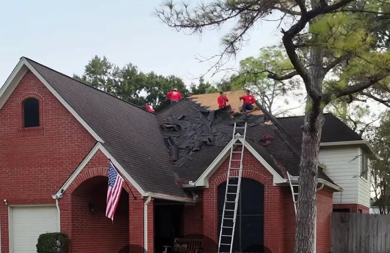 Roofers installing charcoal architectural shingles on brick home with multiple roof planes